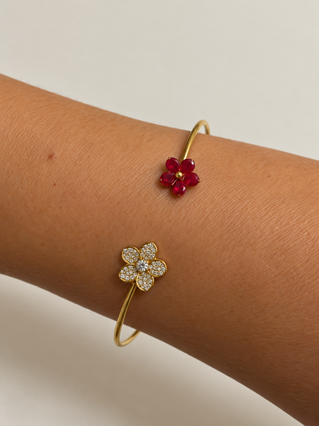 Pulsera Dúo Floral Encantado BRAVATA, detalle 2: pulsera rígida abierta con dos flores en los extremos; una flor con cinco pétalos rojos facetados y centro dora