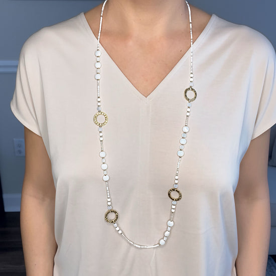 Collar largo dorado con cuentas blancas y aros texturizados, baño de oro 18K sobre modelo