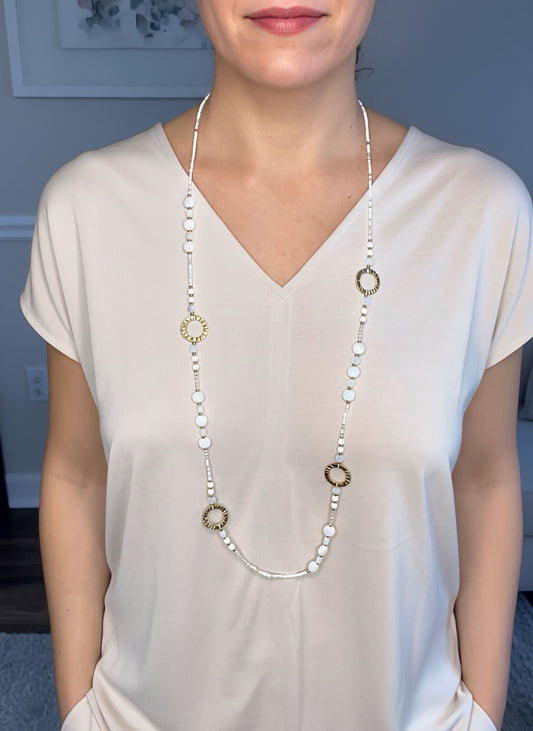 Collar largo dorado con cuentas blancas y aros texturizados, baño de oro 18K sobre modelo