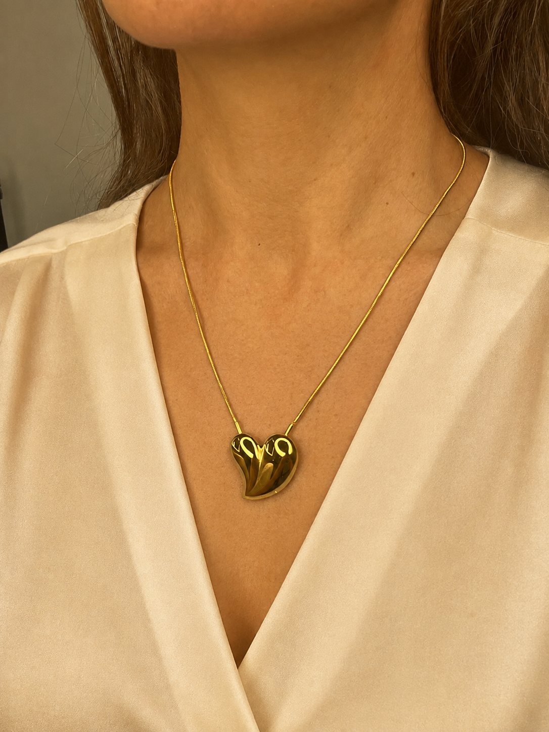 Mujer llevando el Collar Avelon dorado con colgante de corazón irregular.