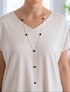 Collar lariat dorado con discos negros esmaltados en acero con baño de oro sobre modelo