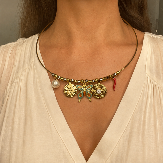 Mujer llevando el Collar Velaria dorado con mariposa, perla y charms decorativos.