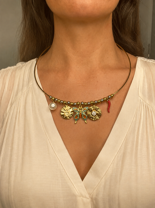 Mujer llevando el Collar Velaria dorado con mariposa, perla y charms decorativos.