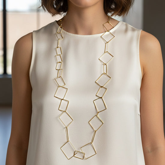Collar largo dorado de eslabones geométricos calados en forma de rombos y cuadrados sobre modelo