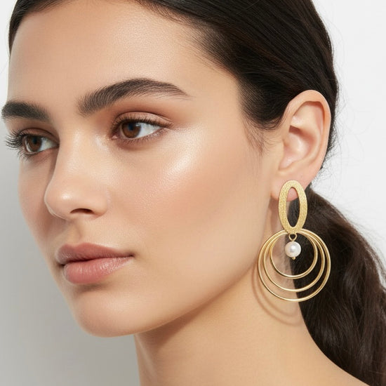 Pendientes dorados con triple aro concéntrico y perla blanca; pieza superior oval texturada (modelo Armonía Perla) sobre modelo