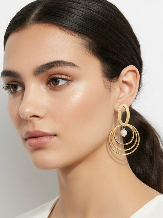 Pendientes dorados con triple aro concéntrico y perla blanca; pieza superior oval texturada (modelo Armonía Perla) sobre modelo