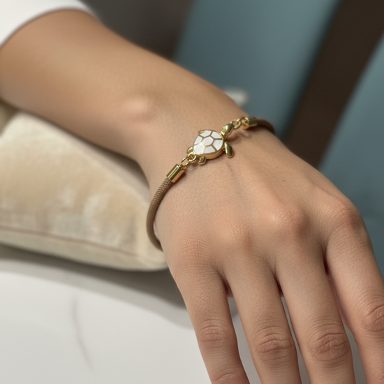 Pulsera Bravata de cordón arena con tortuga dorada y esmalte blanco expuesta en modelo