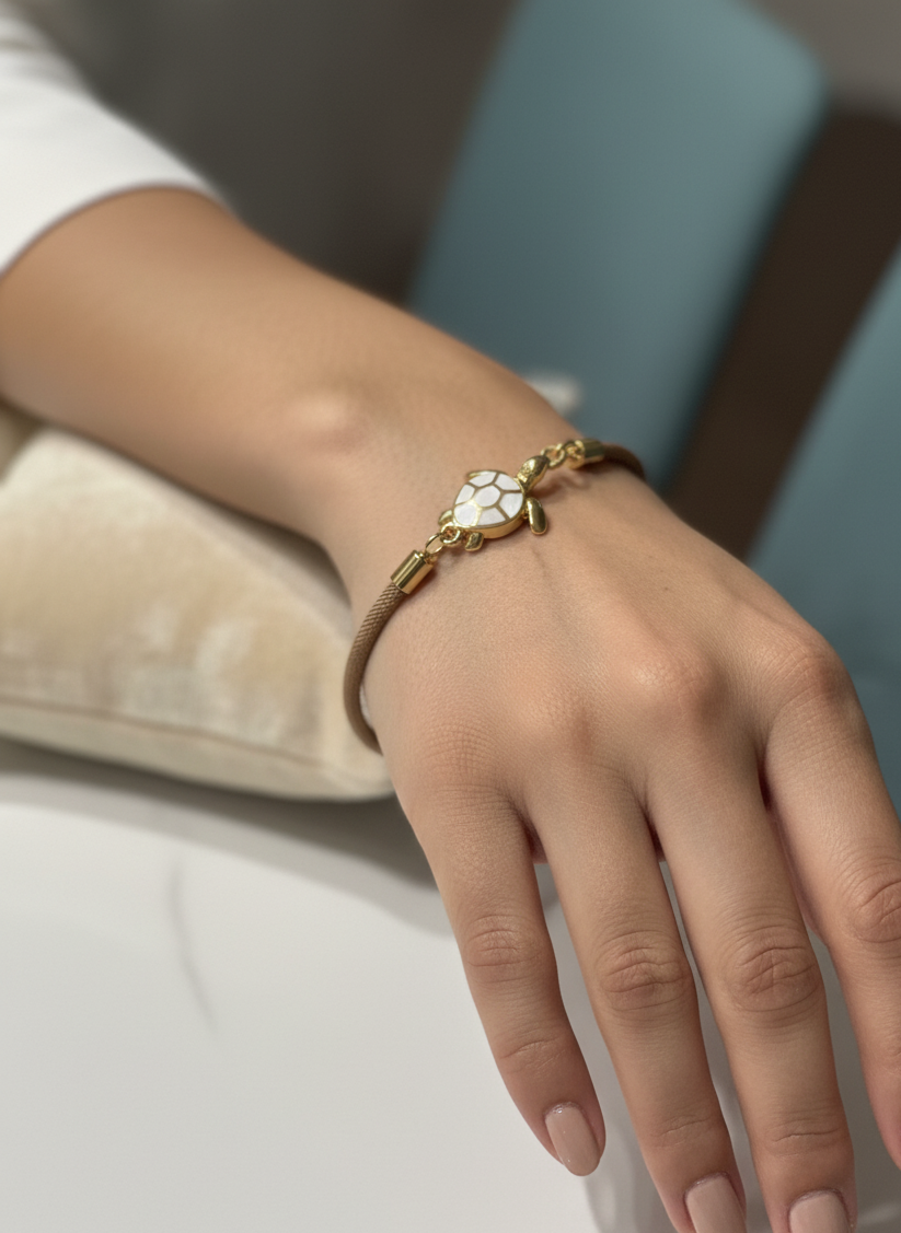 Pulsera Bravata de cordón arena con tortuga dorada y esmalte blanco expuesta en modelo