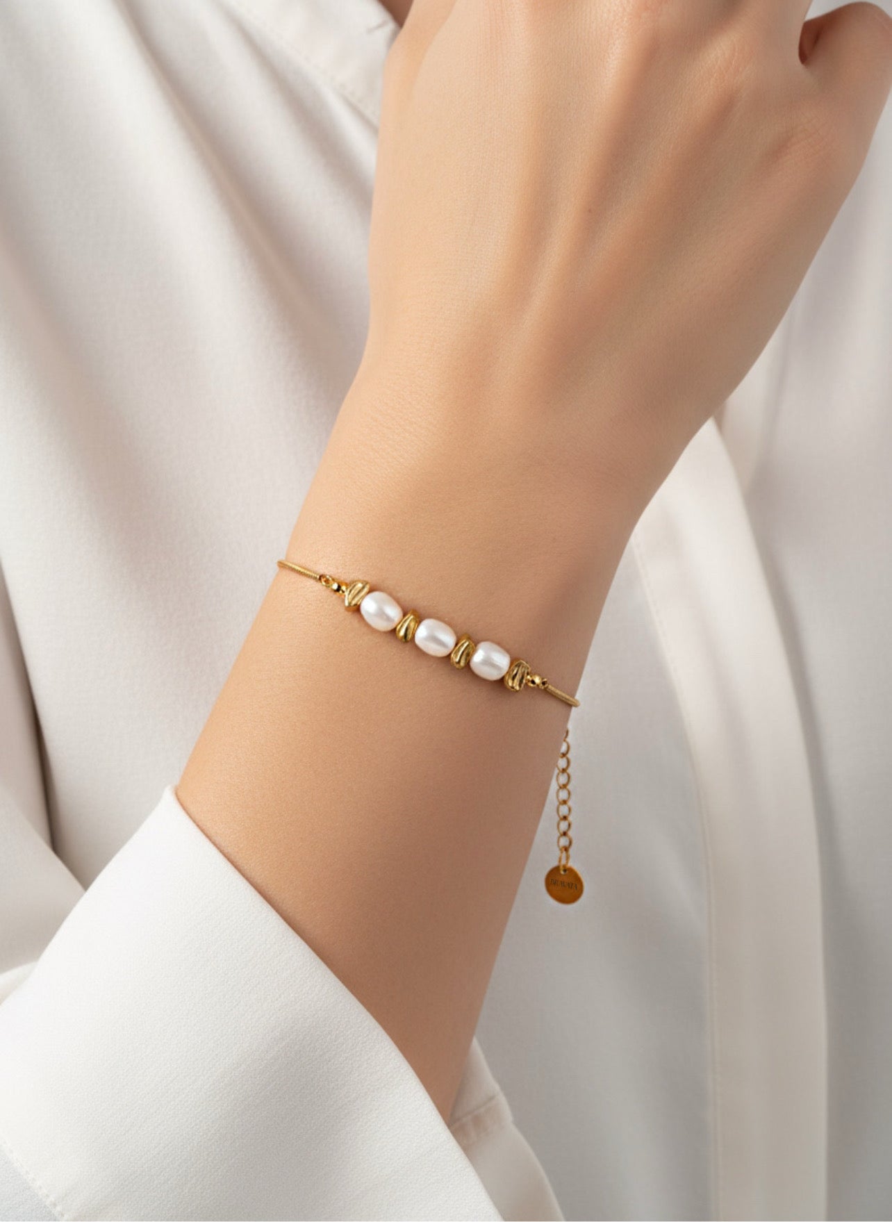 Pulsera Duna dorada con perlas blancas y cuentas irregulares en acero inoxidable con baño de oro 18K sobre modelo