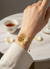 Pulsera dorada con flor grande texturada, en acero con baño de oro 18K sobre modelo