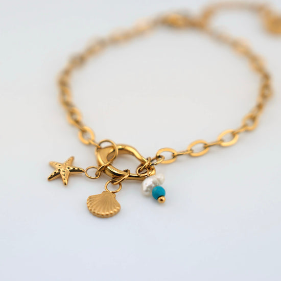 Pulsera Sueños de Sal dorada con charms (estrella de mar, concha y perla con cuenta turquesa) en acero inoxidable con baño de oro 18K