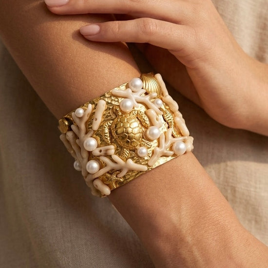 mujer llevando brazalete dorado ancho con tortuga coral blanco y perlas elegante