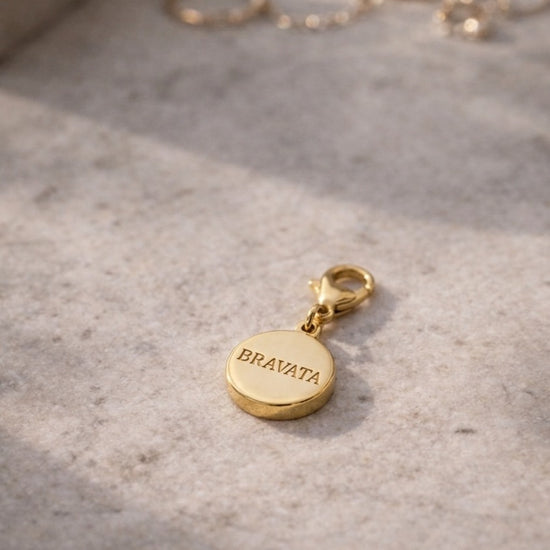 Charm dorado Bravata con grabado del logo en la parte trasera