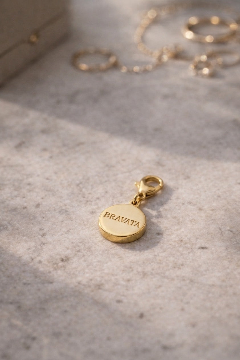 Charm dorado Bravata con grabado del logo en la parte trasera