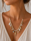 Mujer llevando collar dorado con abalorios blancos y charms inspirados en el mar de BRAVATA