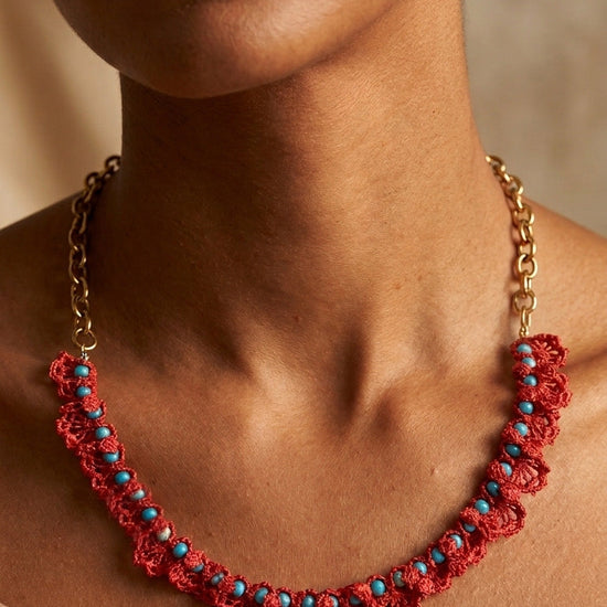 Collar artesanal de crochet en color coral con detalles de turquesas sobre modelo