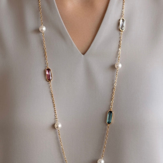 Mujer con collar largo dorado con piedras de colores y perlas Bravata