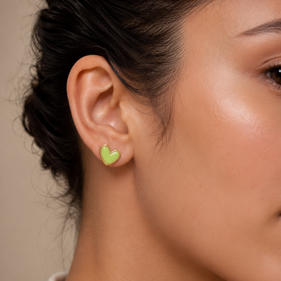 Mujer luciendo los Pendientes Corinne dorados con corazón verde lima