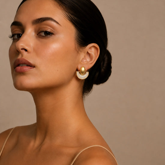 Mujer luciendo pendientes dorados geométricos semicirculares con detalle de nácar blanco, diseño elegante y moderno