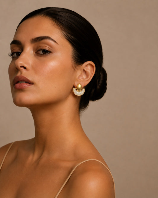 Mujer luciendo pendientes dorados geométricos semicirculares con detalle de nácar blanco, diseño elegante y moderno