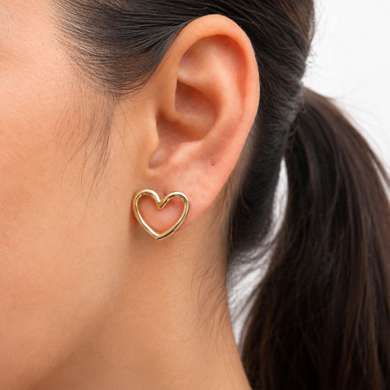 Mujer luciendo los Pendientes Lyssa dorados con diseño de corazón abierto