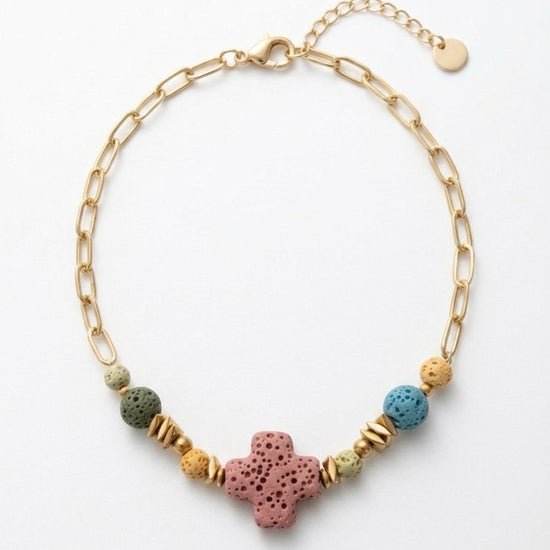Pulsera dorada con cruz central de piedra volcánica y cuentas de colores. Diseño único, moderno y con estilo boho para mujer