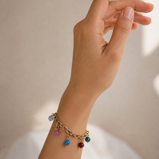 Pulsera dorada con colgantes de colores en muñeca de mujer estilo elegante y veraniego Bravata