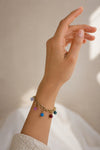 Pulsera dorada con colgantes de colores en muñeca de mujer estilo elegante y veraniego Bravata