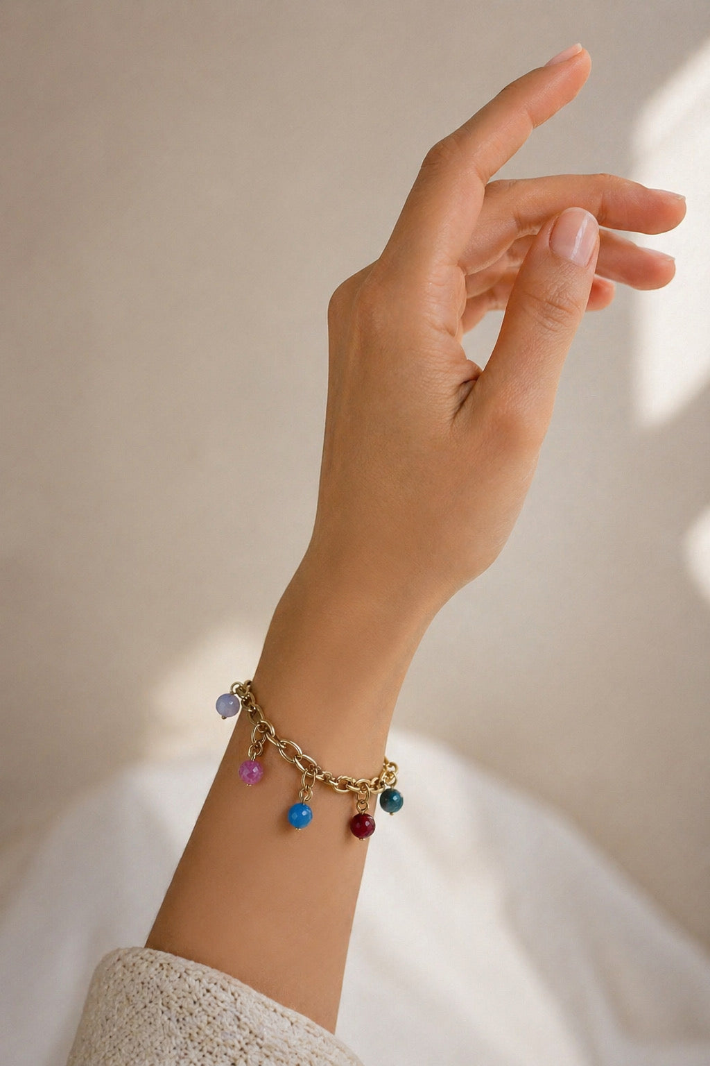 Pulsera dorada con colgantes de colores en muñeca de mujer estilo elegante y veraniego Bravata