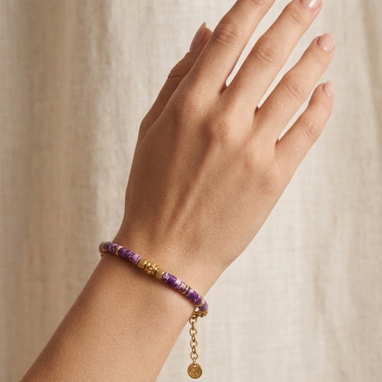 mujer llevando pulsera dorada con cuentas moradas en la muñeca elegante