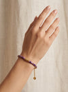 mujer llevando pulsera dorada con cuentas moradas en la muñeca elegante