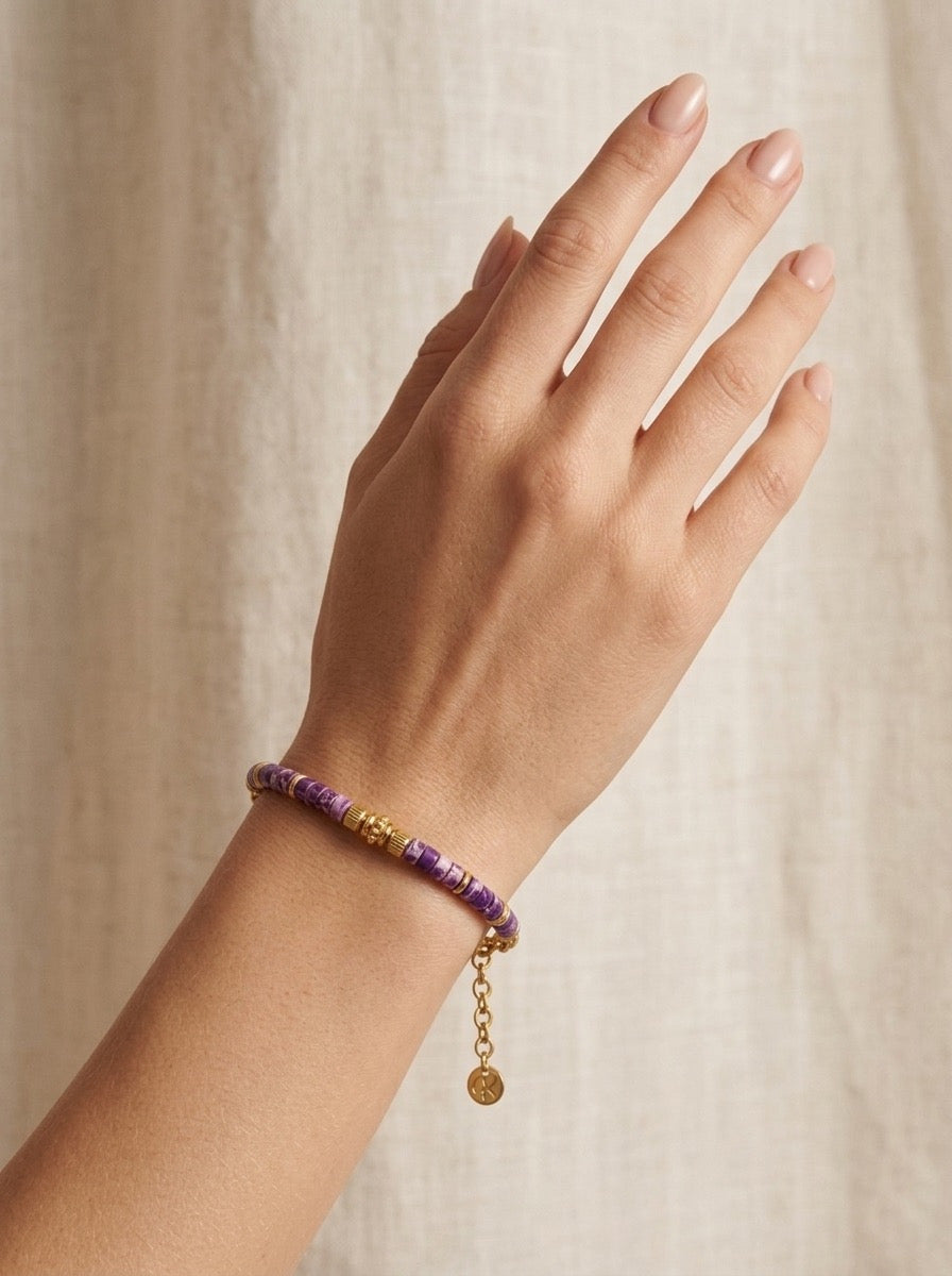 mujer llevando pulsera dorada con cuentas moradas en la muñeca elegante