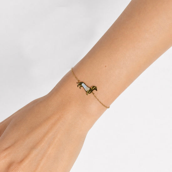 Modelo llevando la Pulsera Tekel dorada con silueta de perro tekel y detalle nacarado blanco de BRAVATA.