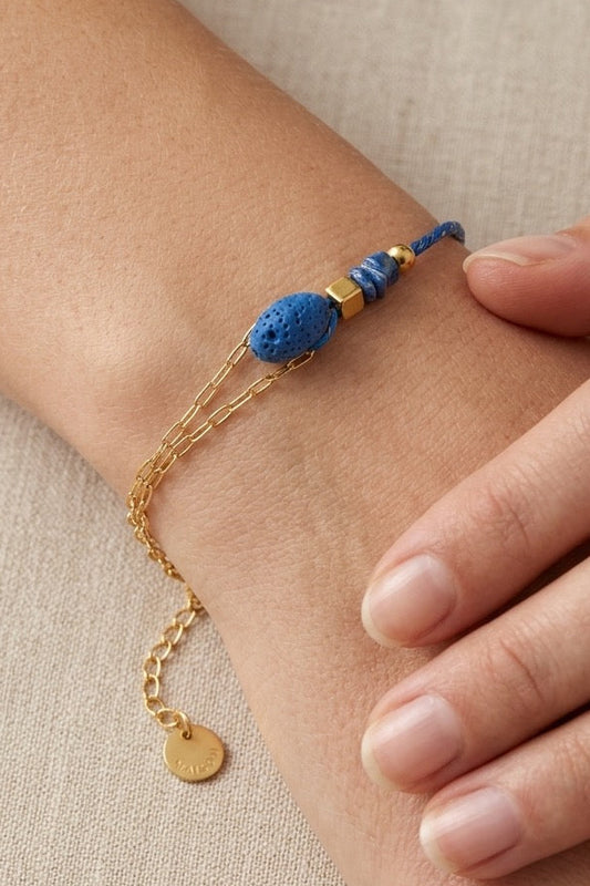 Pulsera con piedra volcánica azul y detalles dorados, llevada en muñeca. Ideal para un estilo natural y actual.